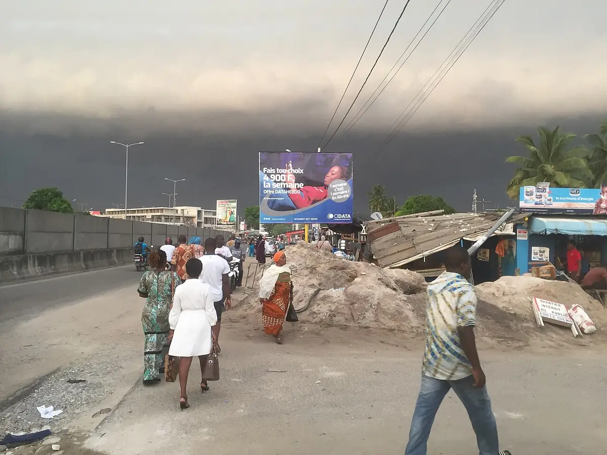 Une rue animée d’Abidjan sous un ciel orageux, avec des passants
