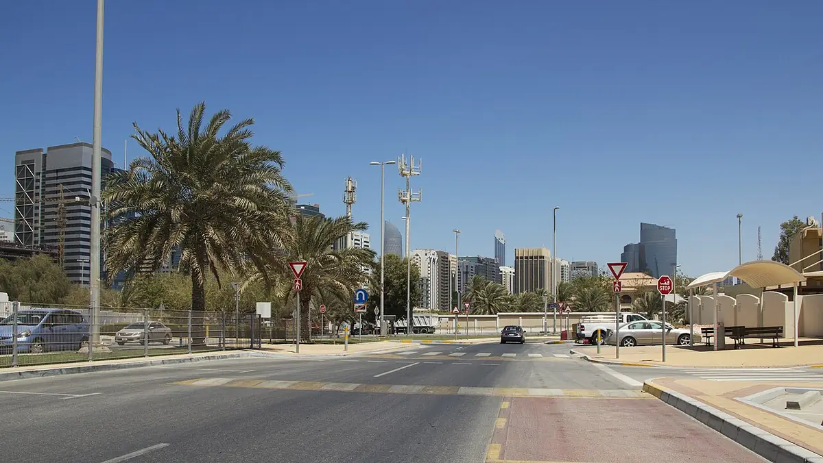 Large avenue d’Abou Dabi avec quelques palmiers, tours en arrière-plan sous un ciel bleu