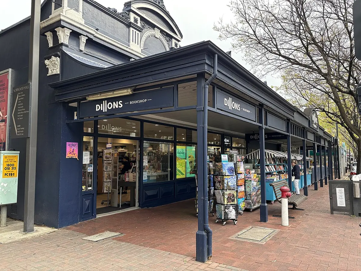 La librairie Dillons, sa véranda au-dessus d'un trottoir en briques, ses présentoirs de cartes postales et les arbres de la rue