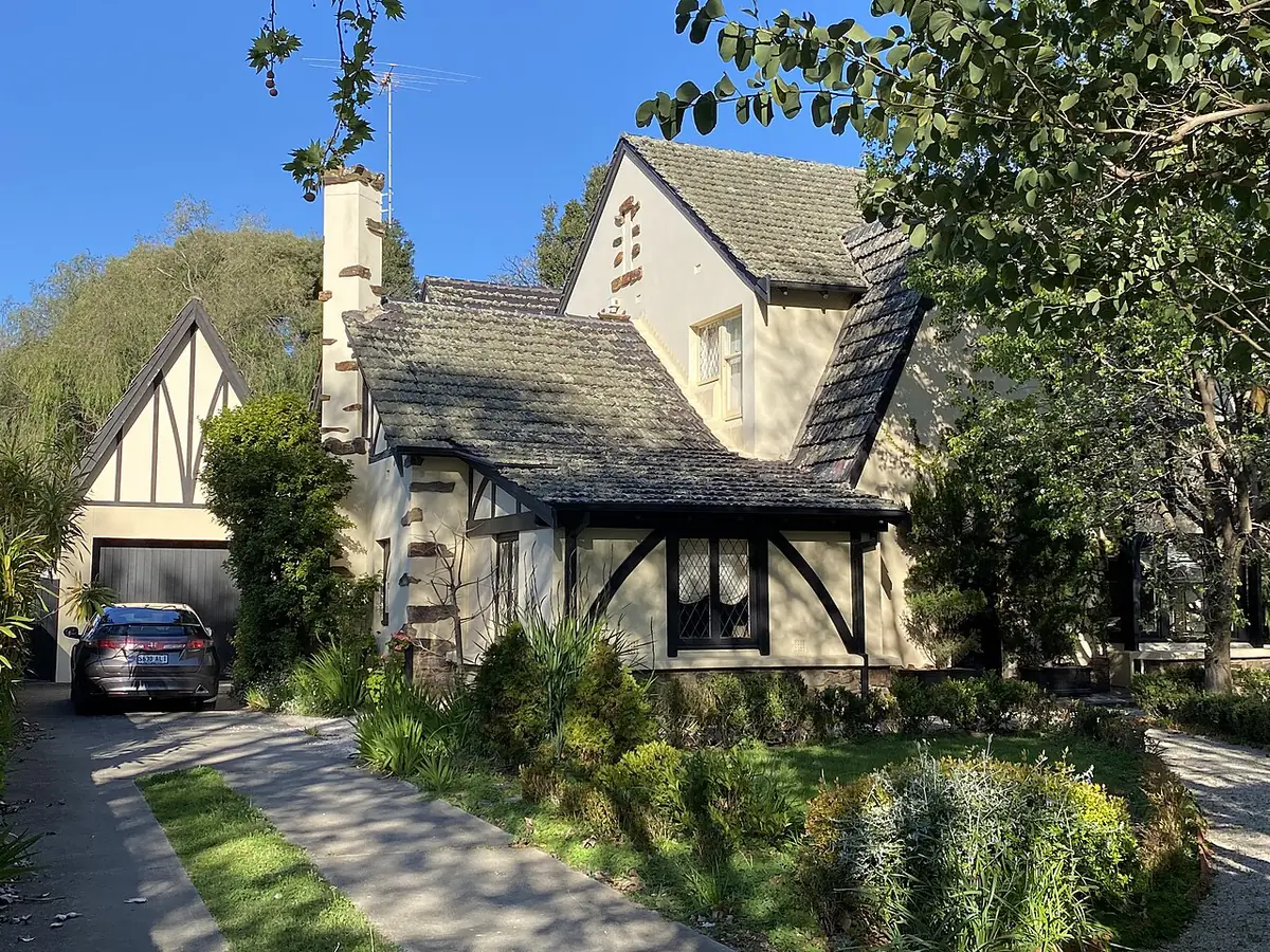 Maison de style néo-Tudor aux pignons pentus, une voiture dans l'allée et un jardin arboré, à Adélaïde