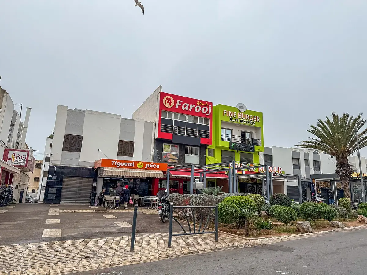 Une rue commerçante à Agadir bordée de magasins et d’un palmier