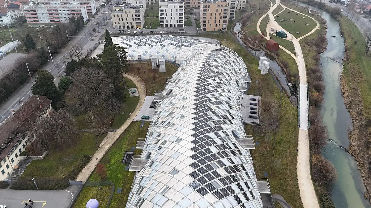 Vue aérienne d’un bâtiment moderne aux courbes audacieuses à Bienne, entouré d’un parc