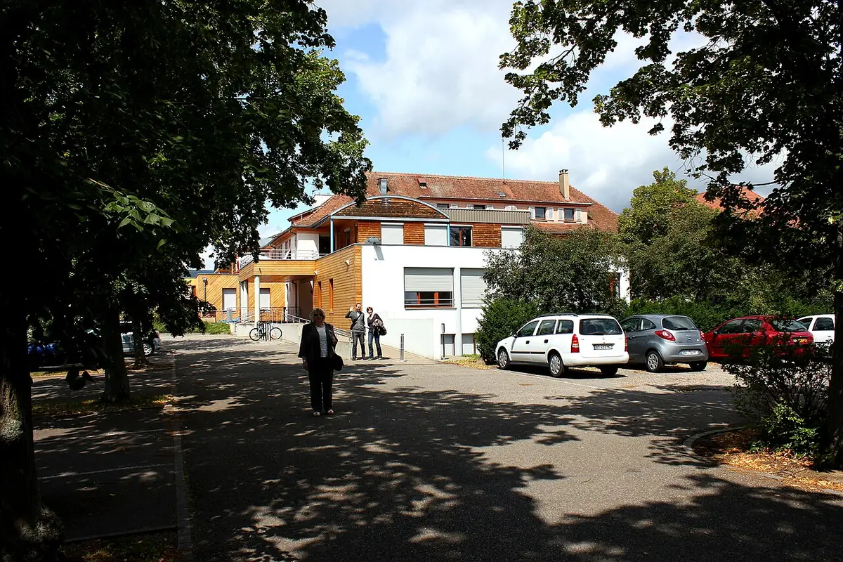 Une allée du parc à Colmar bordée de maisons, promeneurs sur le chemin