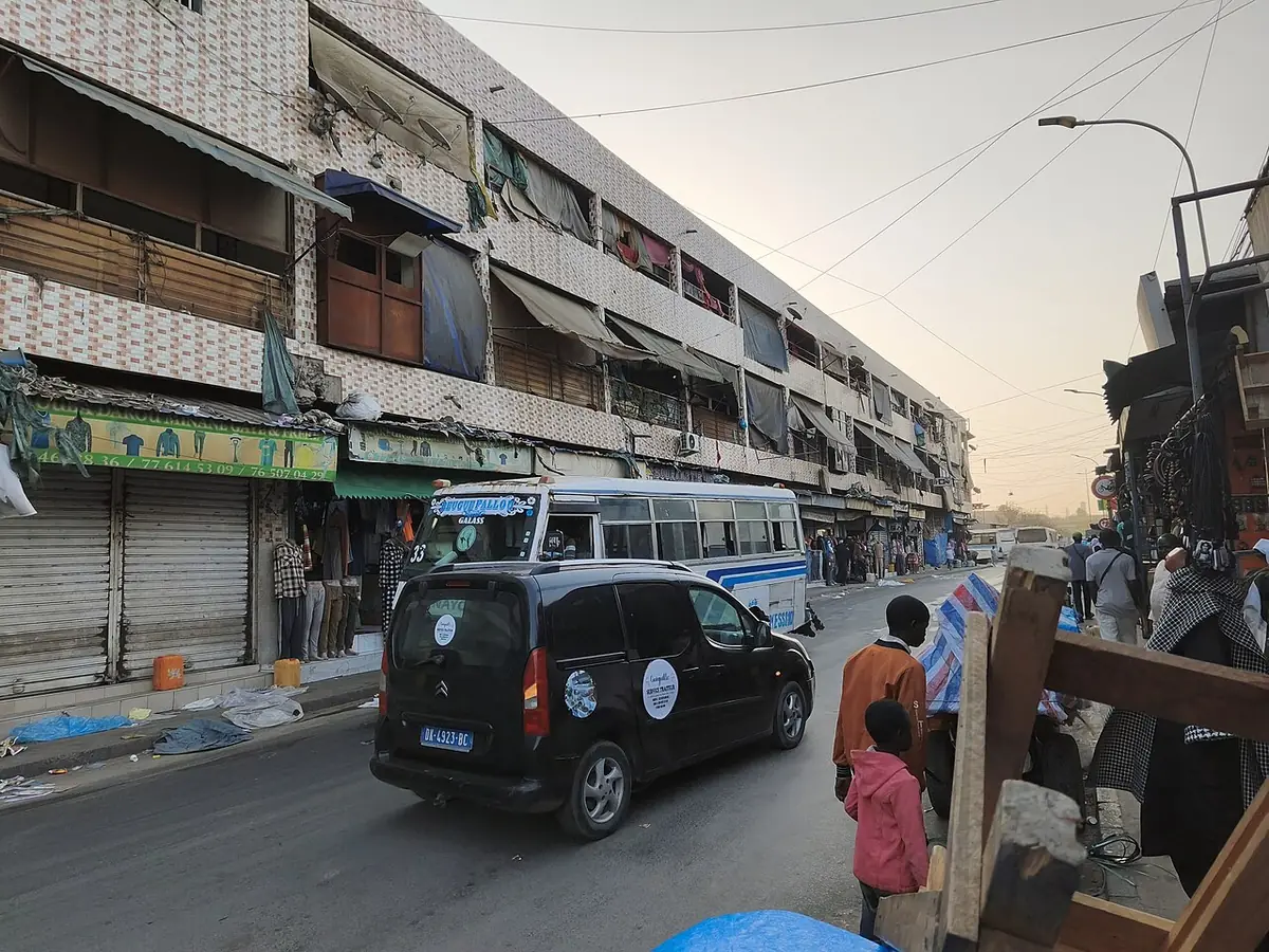 Rue commerçante de Dakar bordée d’immeubles à balcons, avec passants et voitures