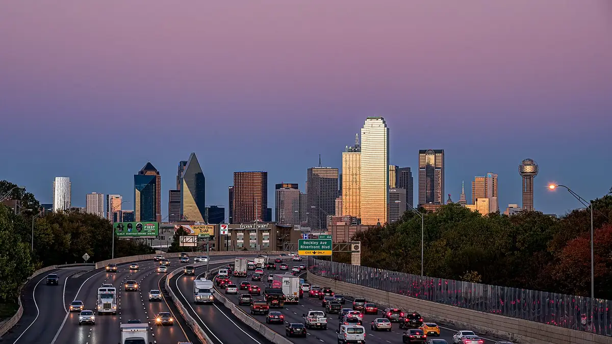 The Dallas skyline at dusk, with a distinctive ball-topped tower and a curving highway below