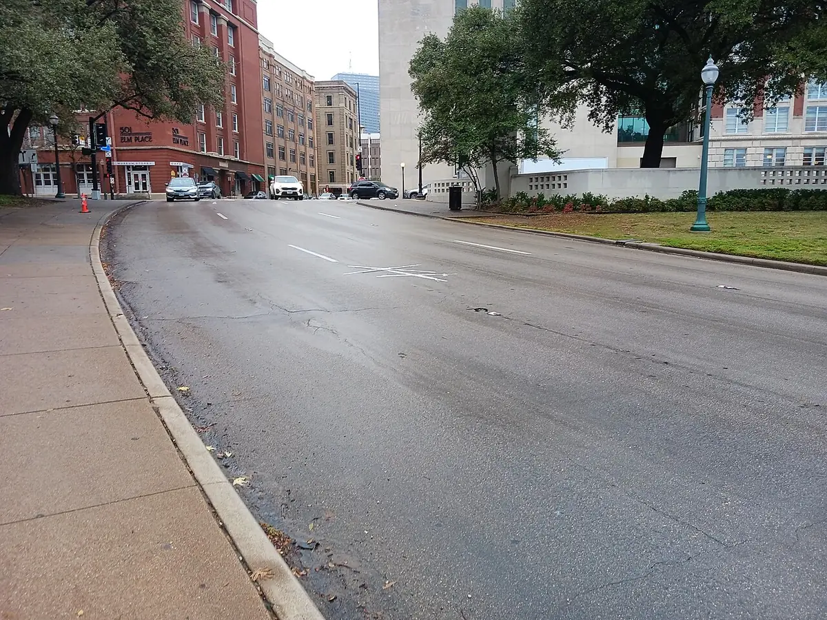 A wide downtown Dallas street lined with a red-brick building and mature trees