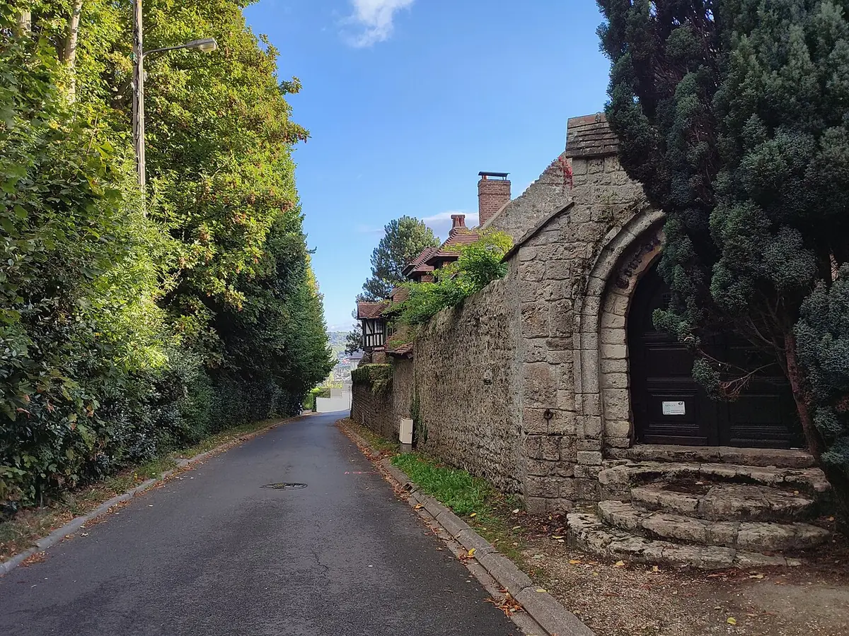 Rue étroite de Deauville entre un mur de pierre et des arbres, sous un ciel bleu