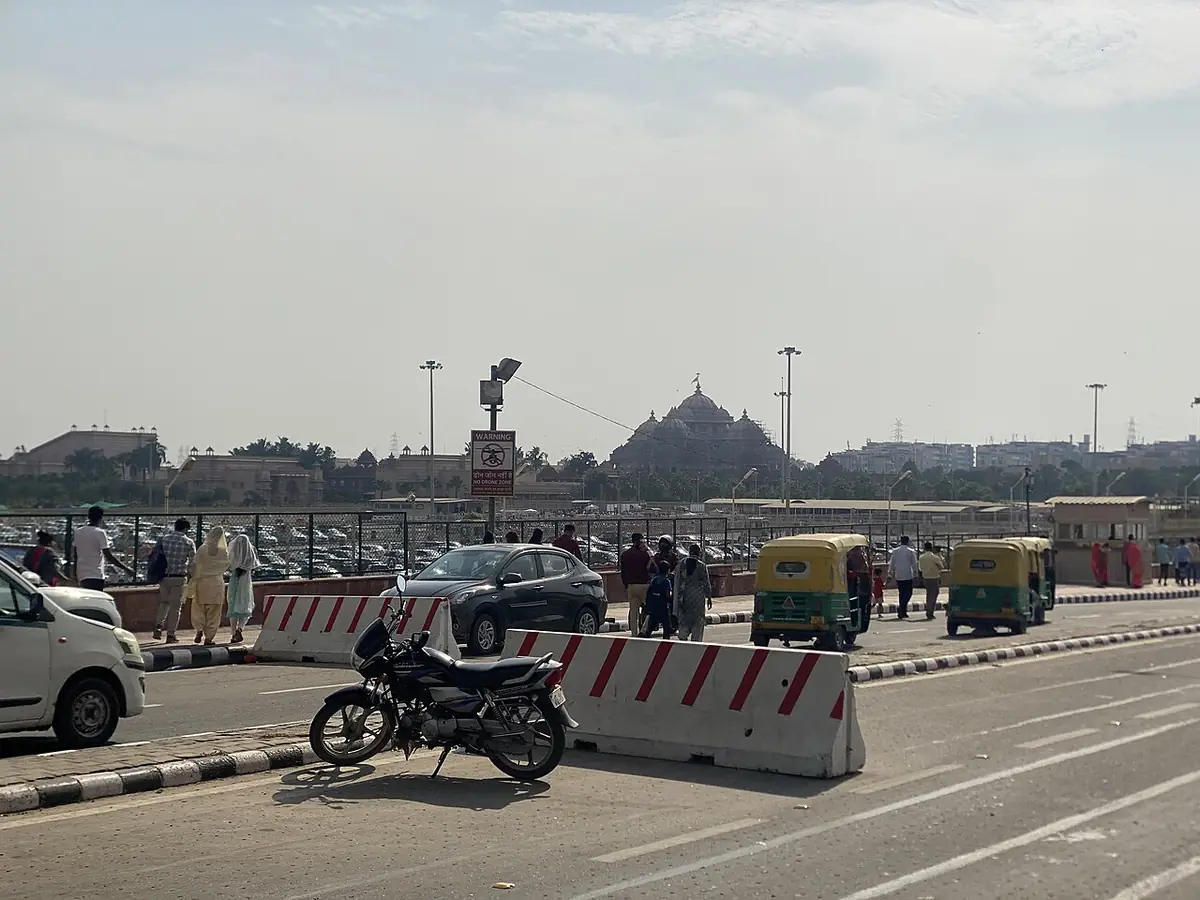 Rickshaws, voitures et motos sur une route de Delhi, avec au loin les dômes du temple d'Akshardham