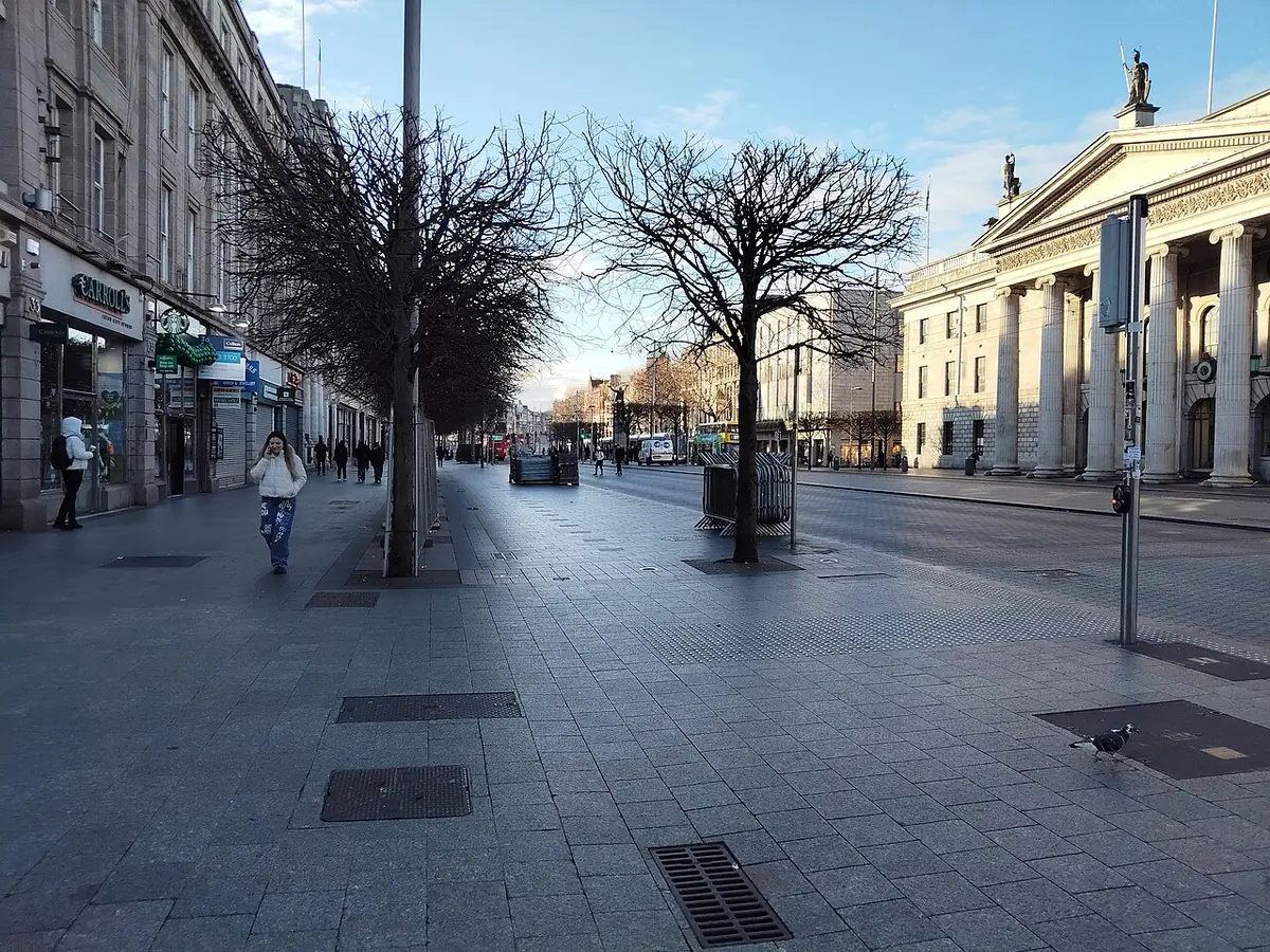 Wide pavement on O'Connell Street, Dublin, with bare trees, shops and a columned facade