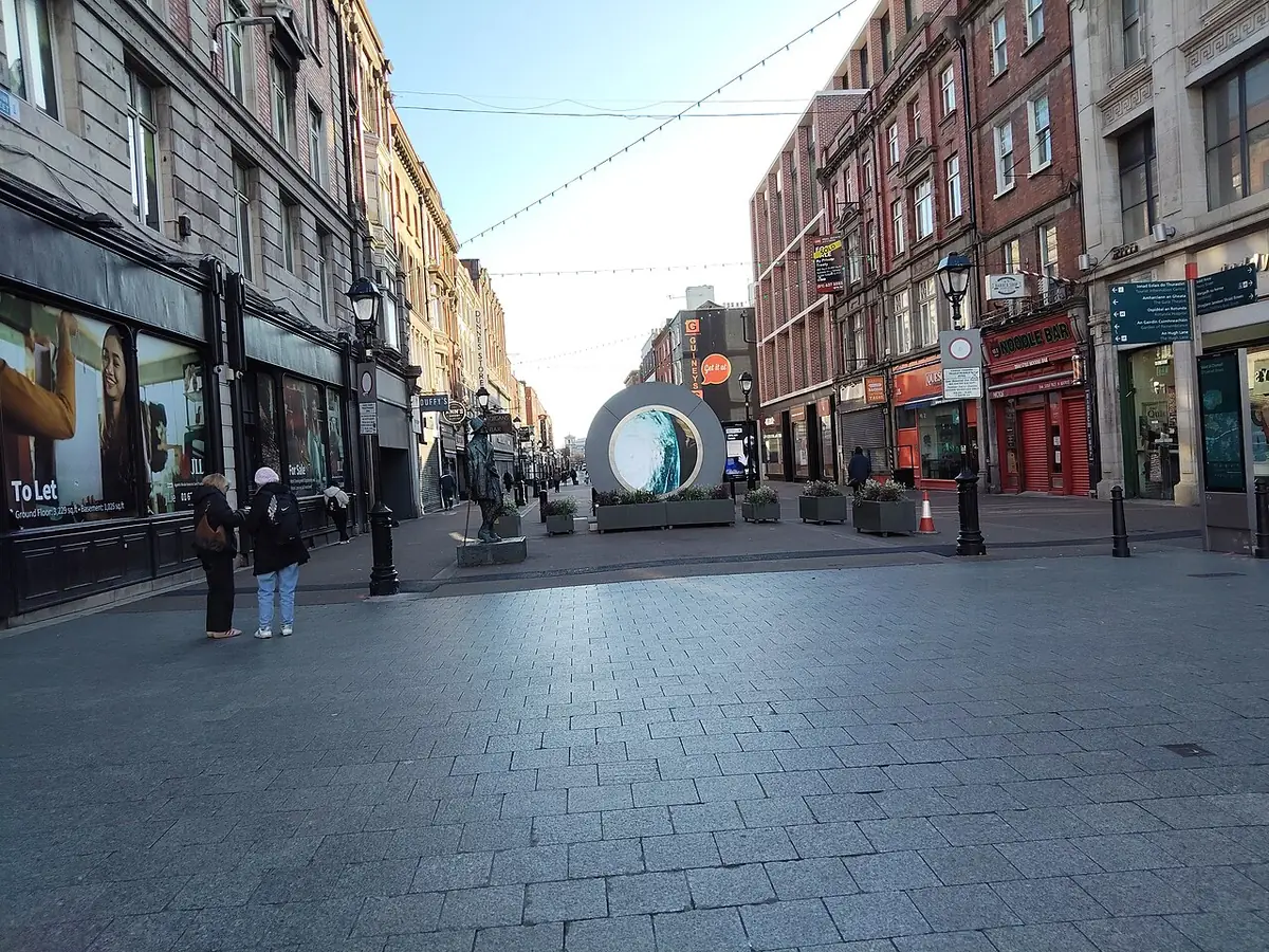 Pedestrianised shopping street in Dublin with the round Portal sculpture, shops and brick buildings
