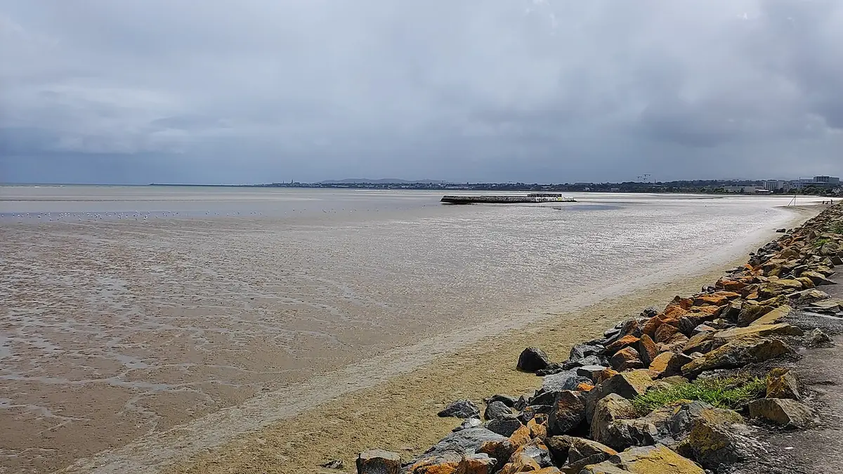 Sandymount Strand in Dublin at low tide, with a rocky shoreline under a cloudy sky