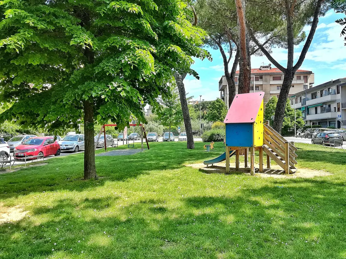 Jardin public arboré avec aire de jeux à Florence, immeubles en arrière-plan