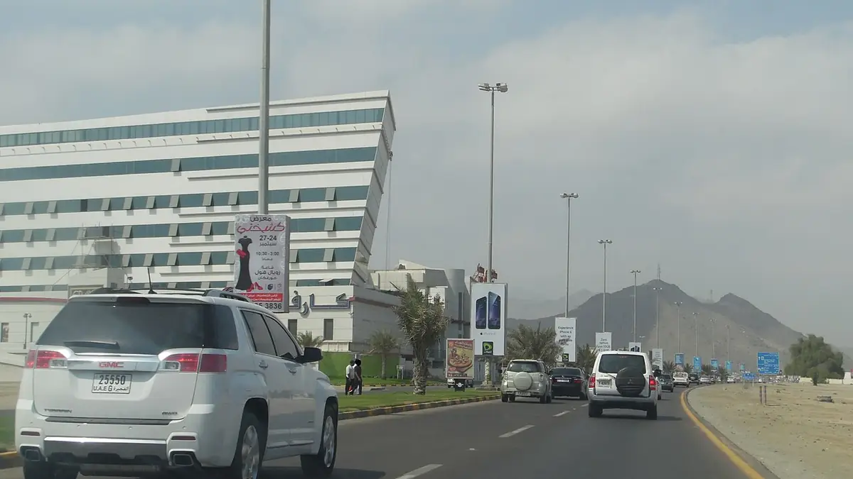 Une route calme traversant Fujairah, bordée d’immeubles, avec des montagnes en arrière-plan