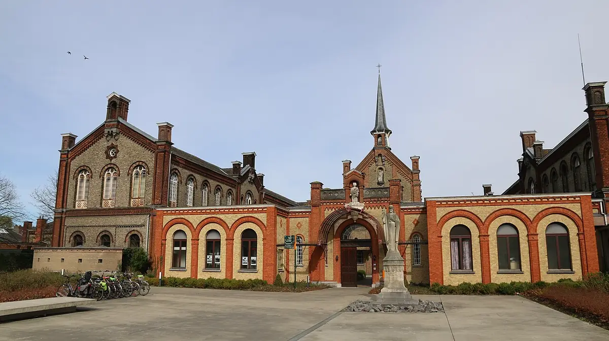 Un imposant bâtiment néogothique en briques rouges à Gand, sous un ciel dramatique