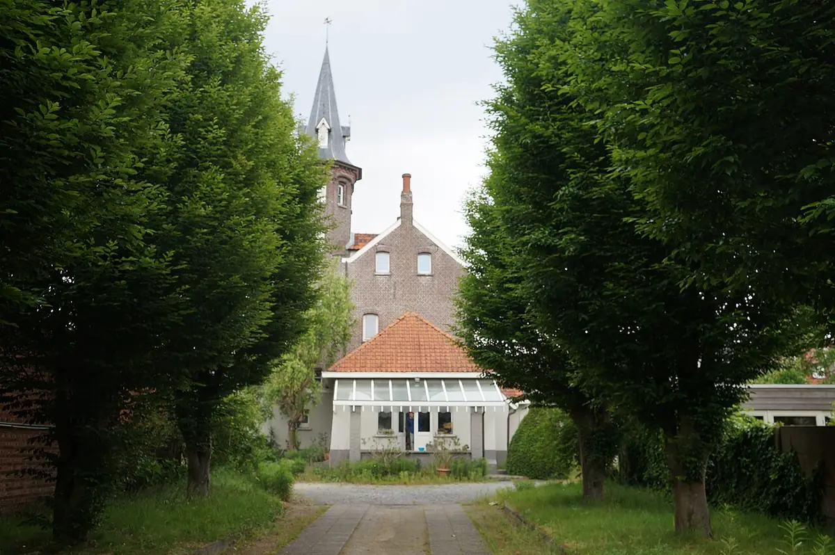 Une allée bordée d’arbres menant à une maison à tourelle à Gand