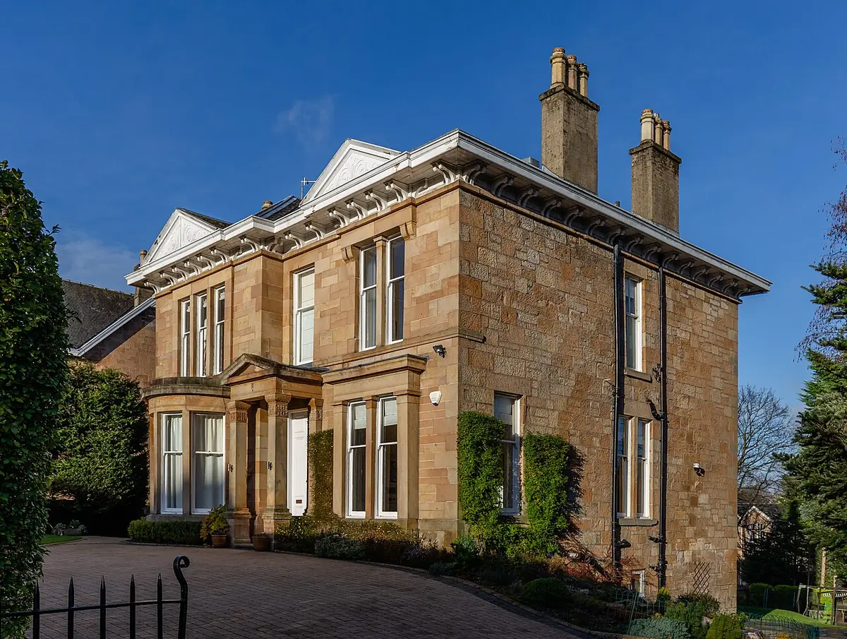 Une villa victorienne en grès, lierre et fenêtres en saillie, derrière une grille en fer