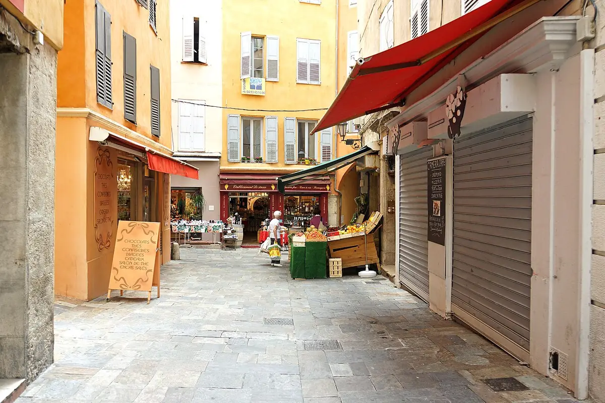 Rue des Quatre-Coins à Grasse, façades ocre, étal de fruits et légumes et stores rouges