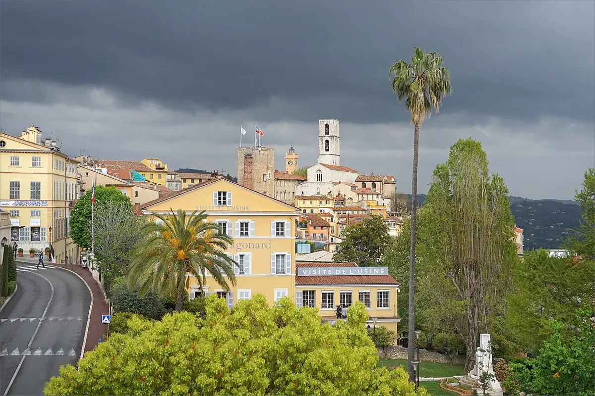 Vue sur la vieille ville de Grasse et son clocher sous un ciel d’orage, palmiers au premier plan