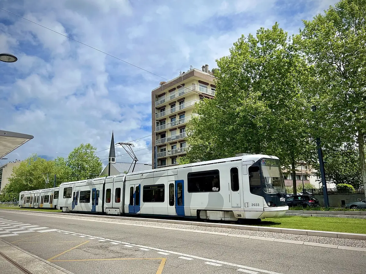 Un tramway passe devant des immeubles et un parc à Grenoble