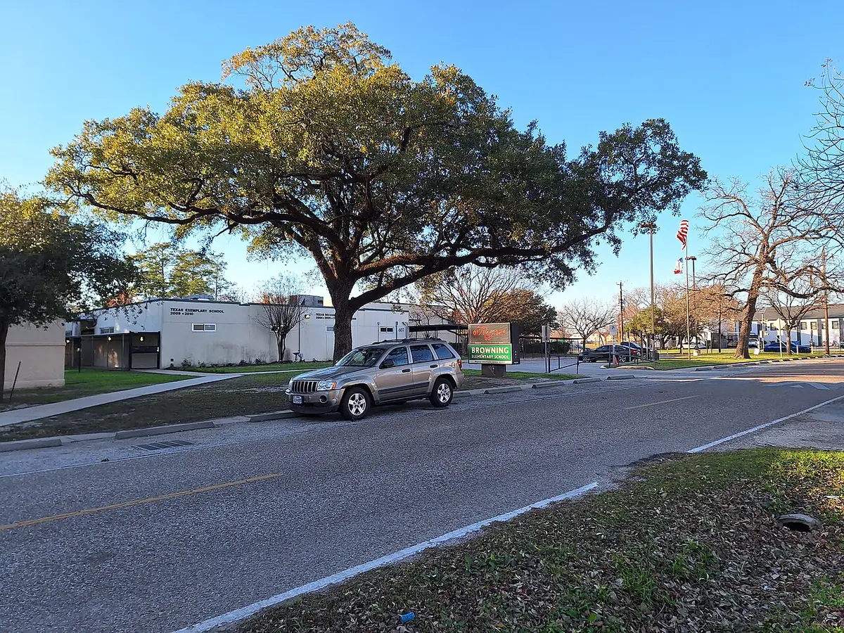 Une rue calme de Houston ombragée par un grand chêne, une voiture qui passe