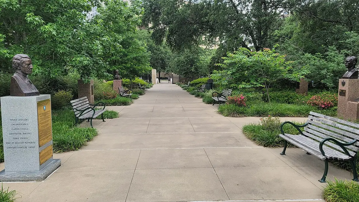 Une allée pavée bordée de bancs et d’arbres aux jardins McGovern Centennial à Houston