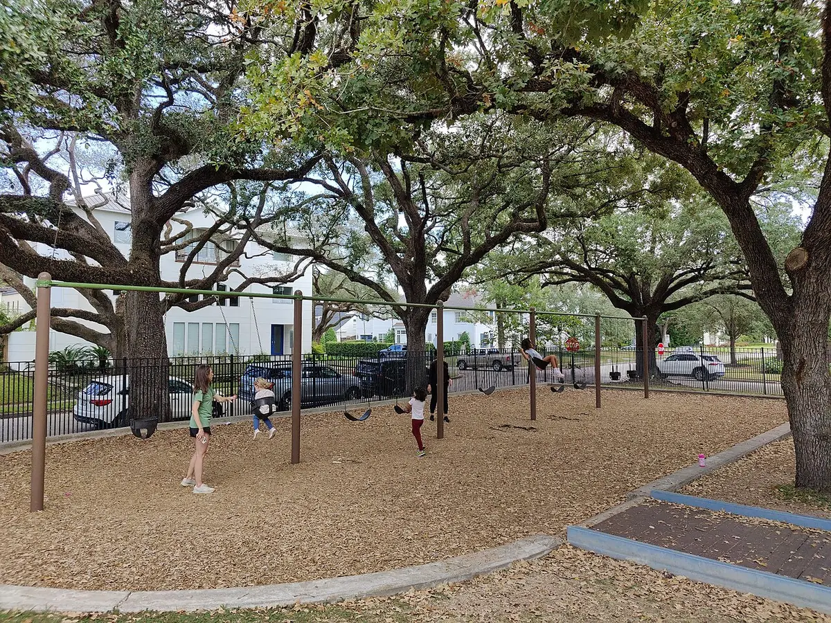 Une aire de jeux avec balançoires sous de grands chênes, dans un parc de Houston