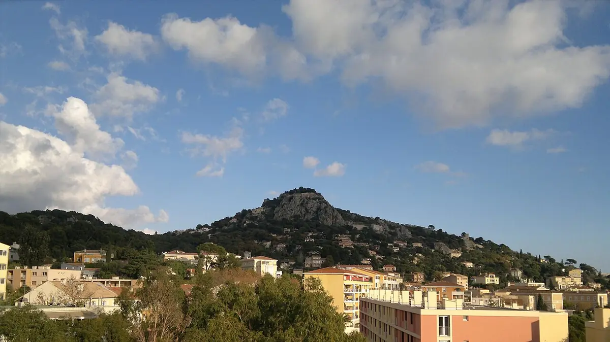 Immeubles d’Hyères au pied d’une colline boisée sous un ciel nuageux