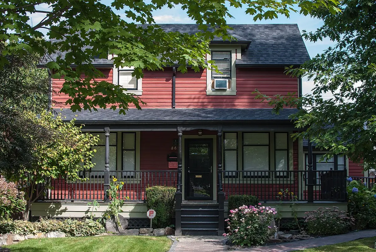 La maison H.C. Cooper à Kelowna, maison en bois rouge avec porche, entourée d’arbres et de fleurs