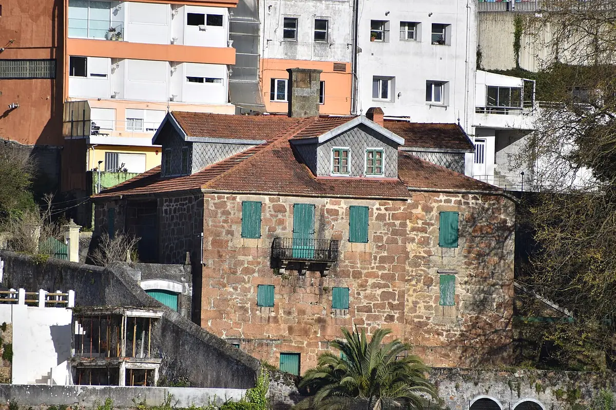 Le pazo de Guyatt, maison en pierre aux volets verts, devant de grands immeubles d’habitation