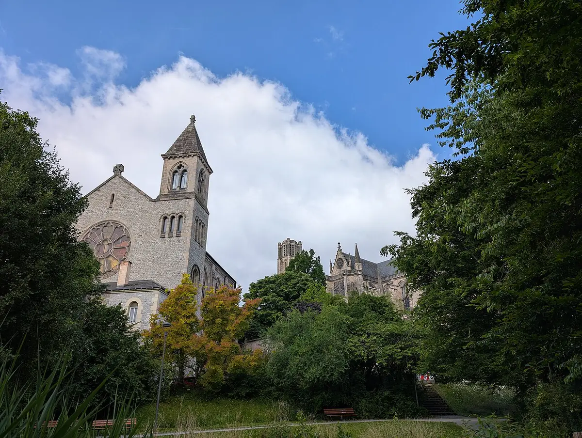 Une église en pierre à clocher dans la verdure, la cathédrale Saint-Étienne de Limoges en arrière-plan