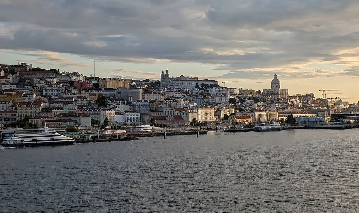 Les collines de Lisbonne couvertes de maisons, vues depuis le Tage sous un ciel nuageux