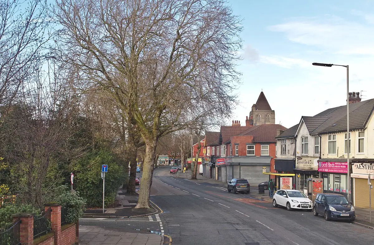 Une rue de Liverpool bordée d’arbres, maisons mitoyennes et commerces au rez-de-chaussée