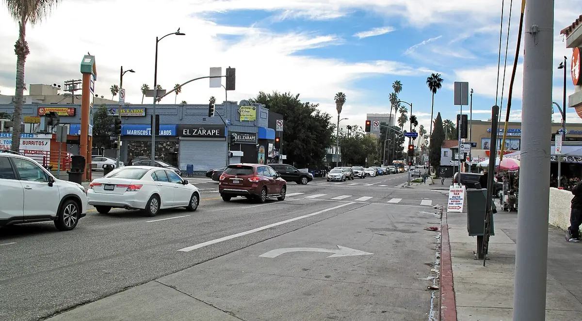 Un coin de rue animé à Los Angeles, avec commerces, voitures garées et palmiers