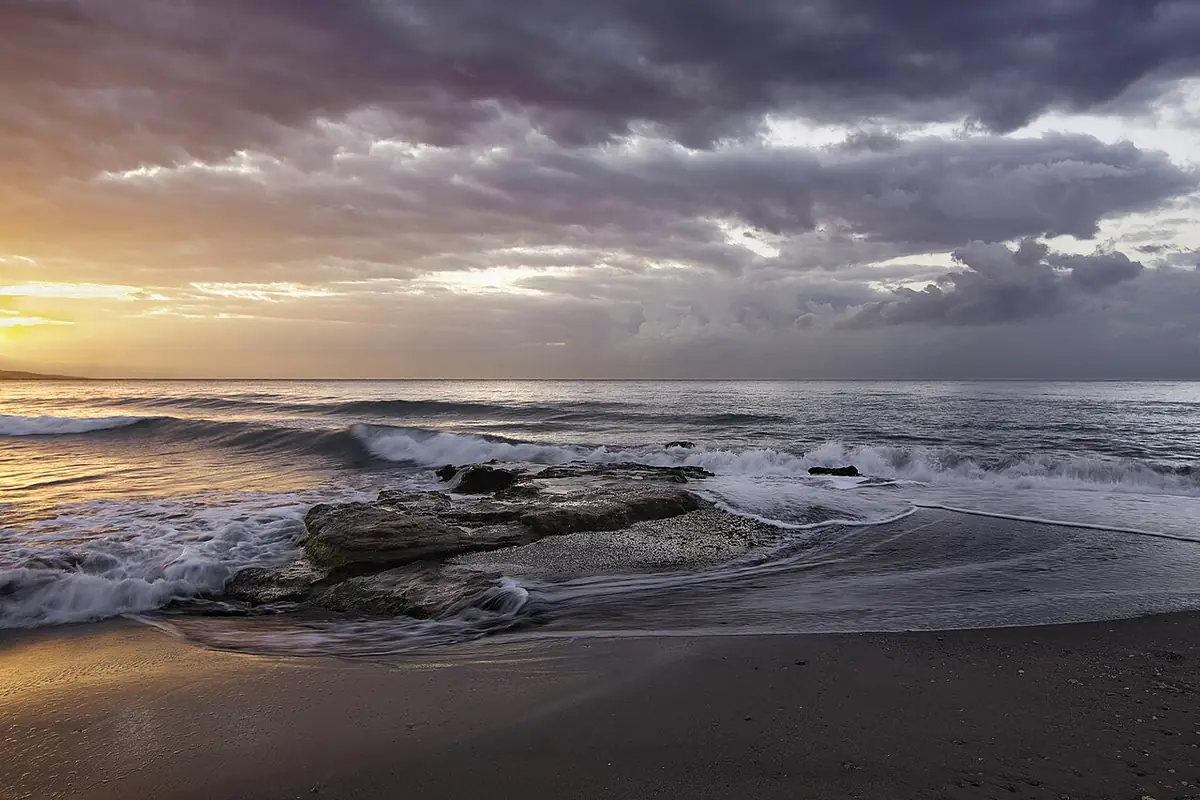 La plage de la Misericordia à Málaga, rochers et ciel orageux au coucher du soleil