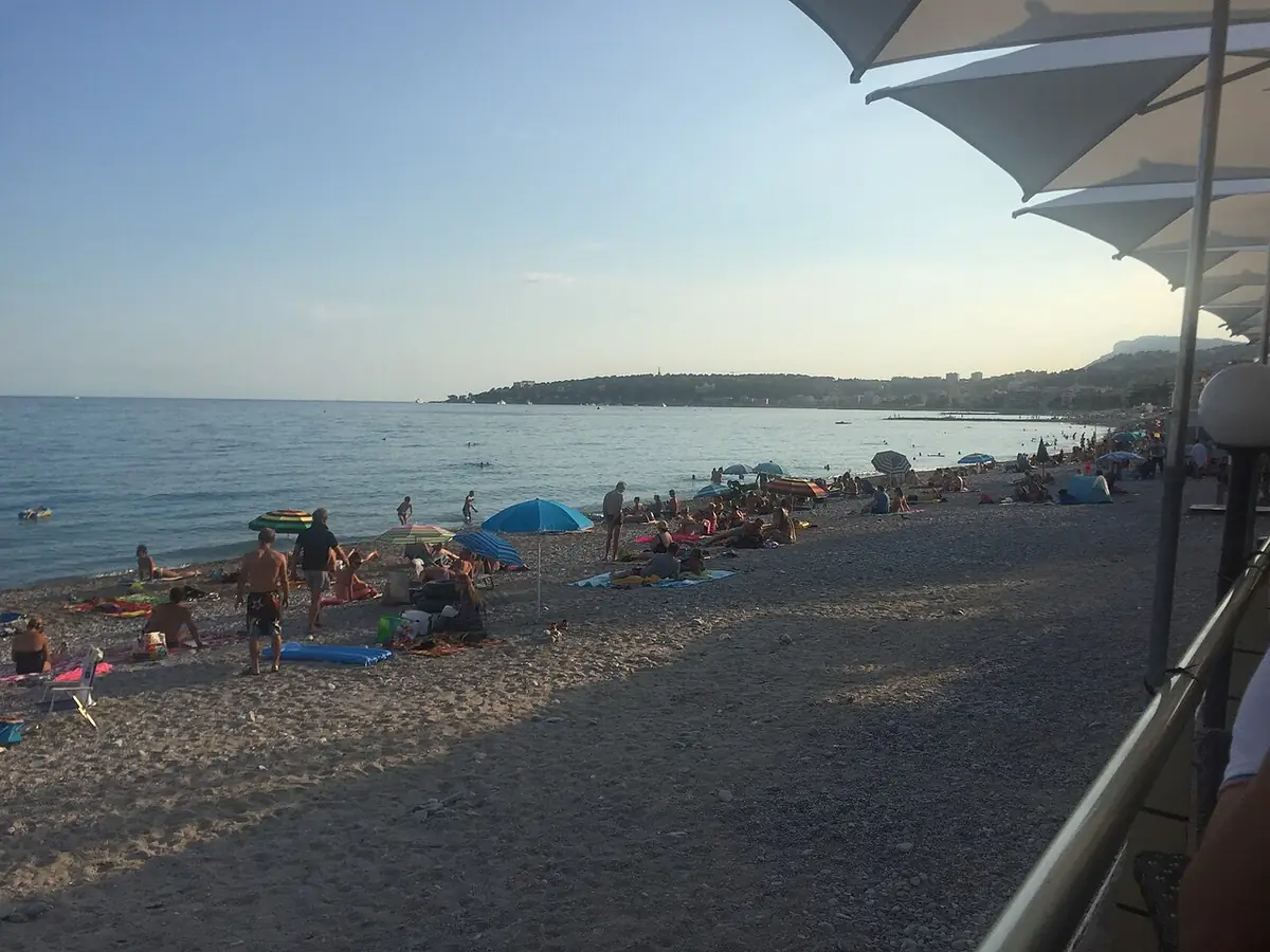 La plage de la baie du Soleil à Menton en fin de journée, avec de nombreux baigneurs, vue depuis une terrasse