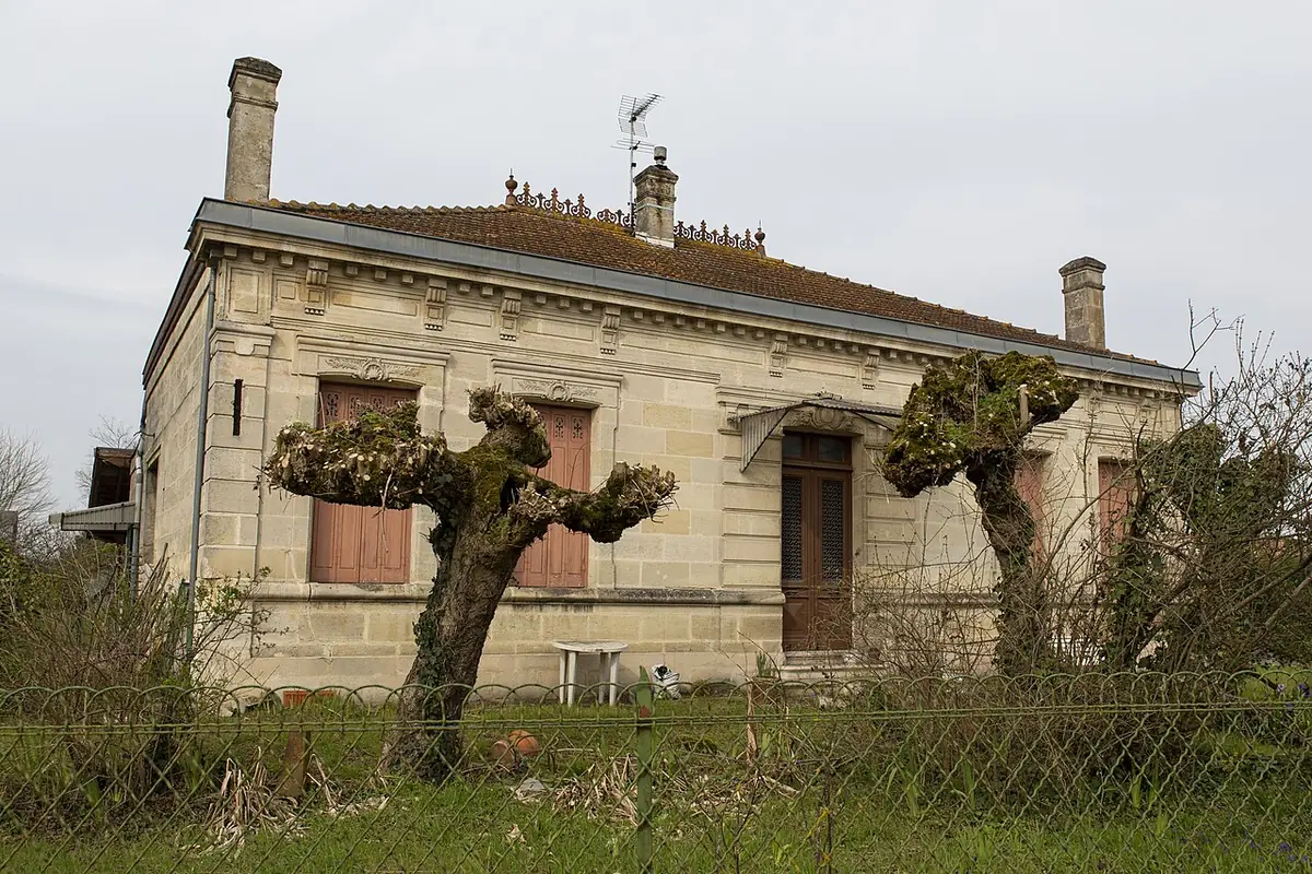 Maison en pierre à Mérignac, volets fermés et arbres taillés devant la façade