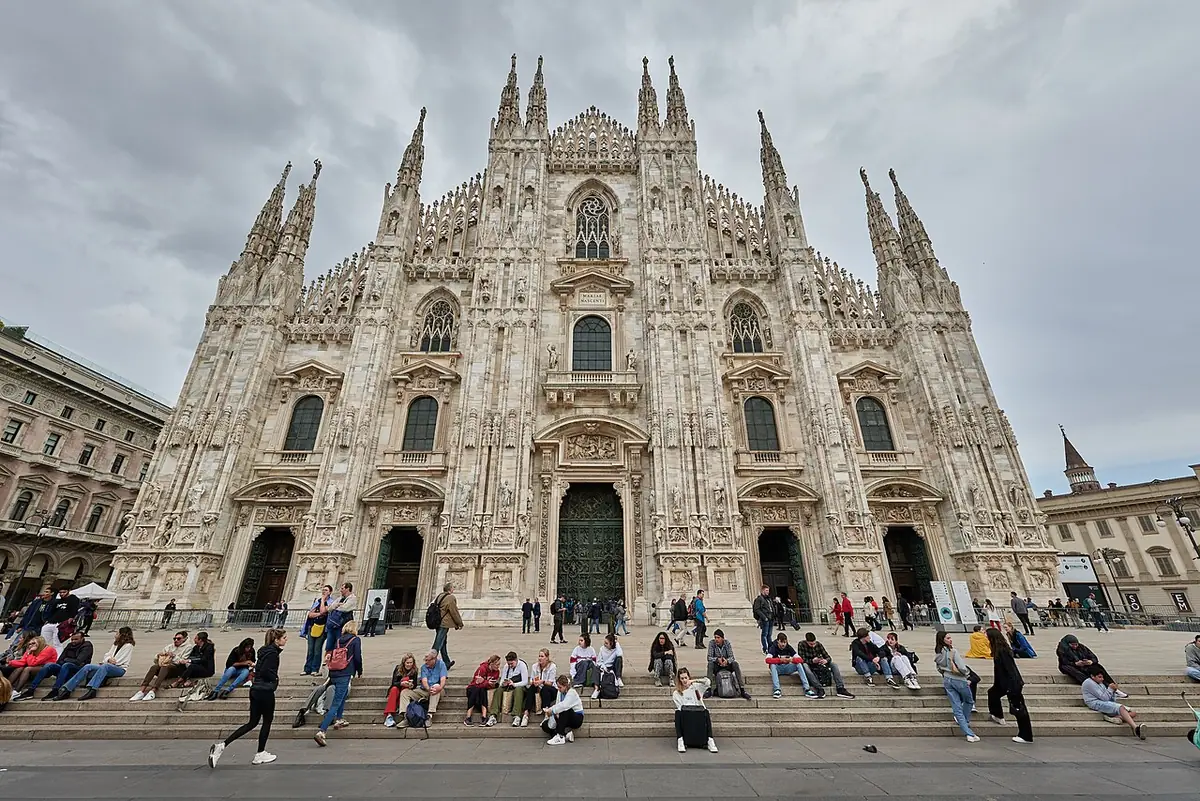 La façade du Duomo de Milan sur la piazza del Duomo, visiteurs assis sur les marches