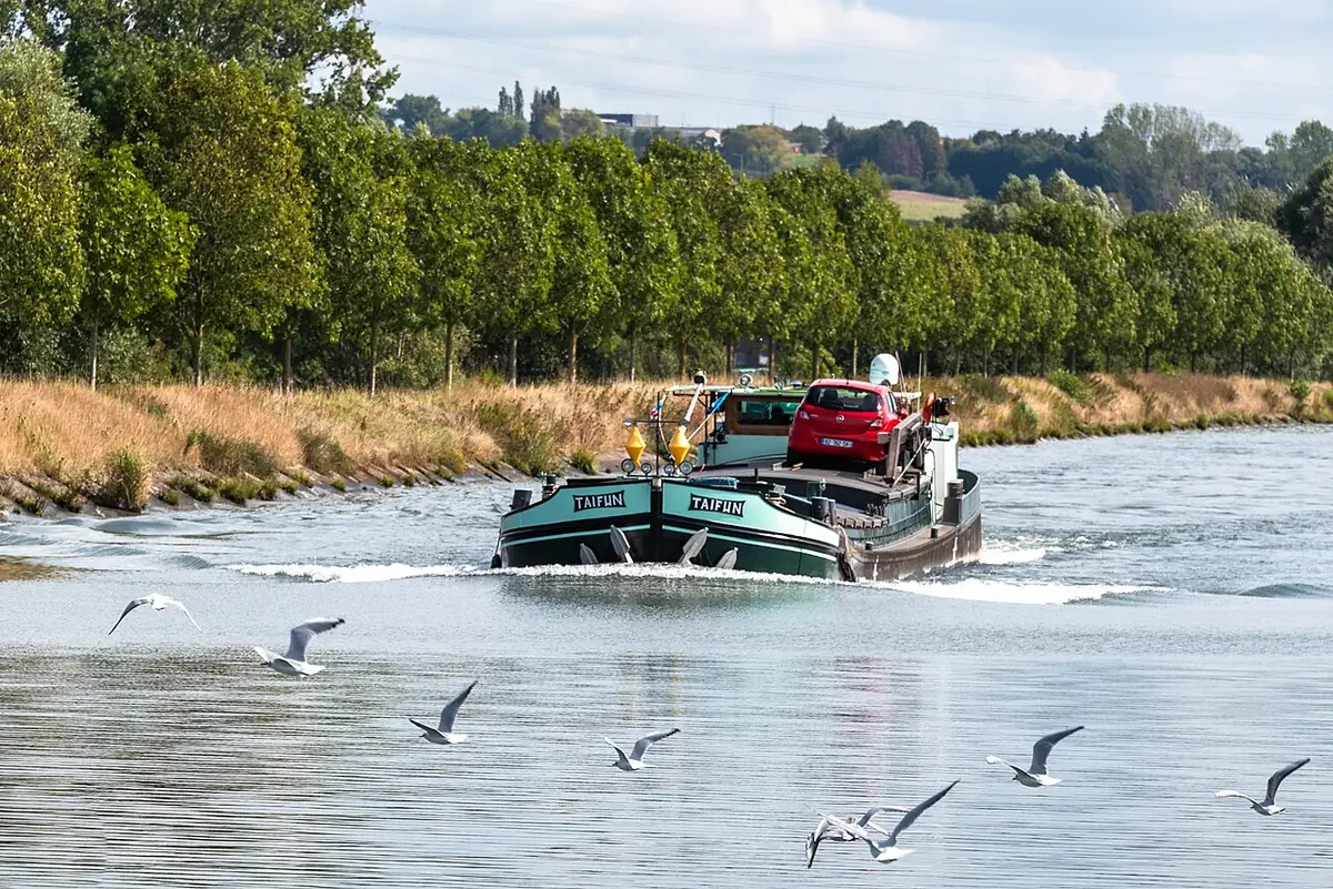 Une péniche navigue sur le canal, oiseaux en vol, à Mons