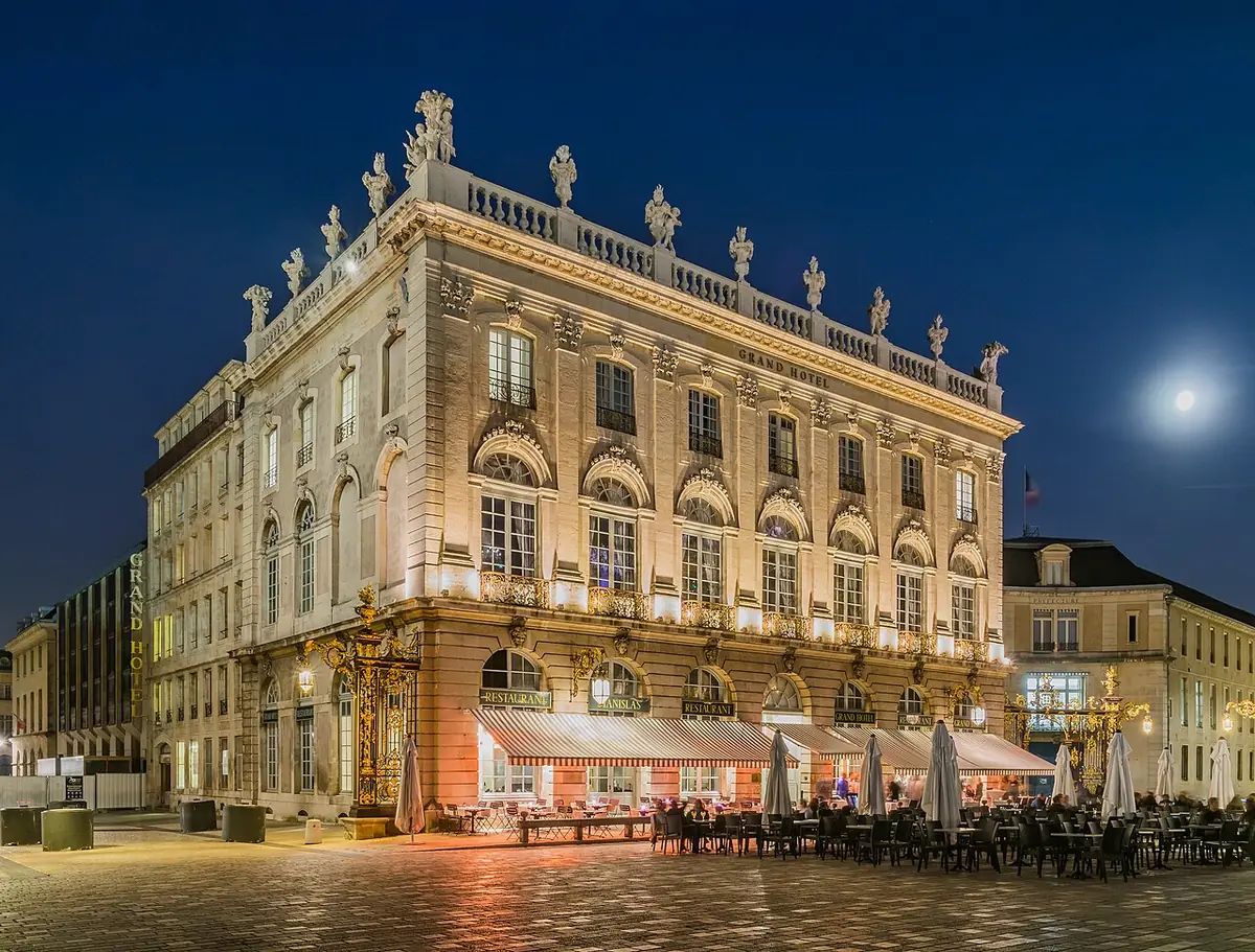 Le Grand Hôtel de Nancy illuminé le soir, terrasses de café au pied de la façade