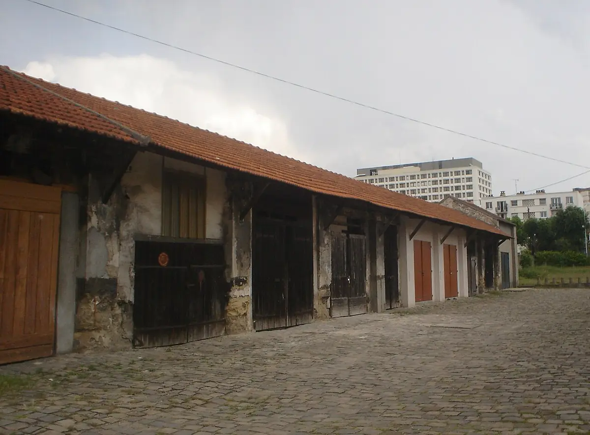 Anciens abattoirs de Nanterre : longue halle aux portes en bois sur une cour pavée, immeubles au fond