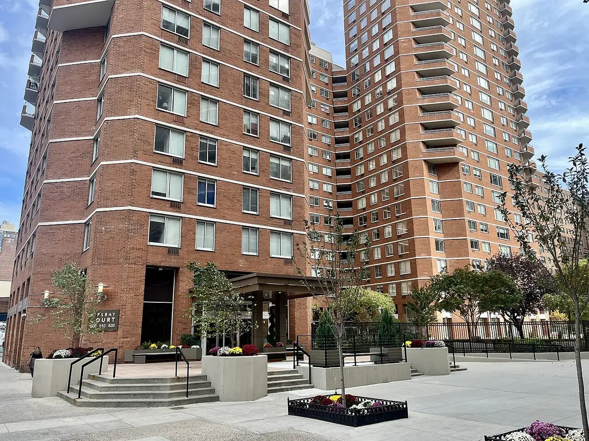 Un grand complexe d’appartements en brique avec une place paysagée devant
