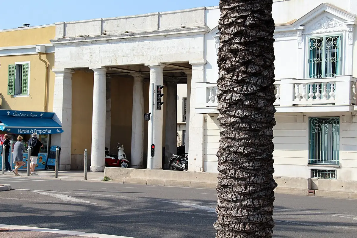 Une rue du Vieux-Nice bordée d’un immeuble à colonnes et de palmiers