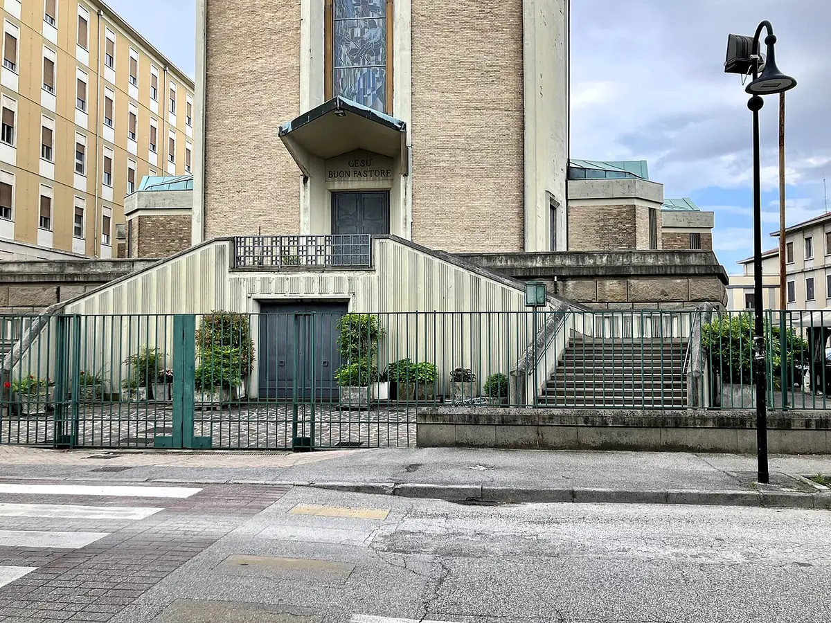 Façade de l’église Gesù Buon Pastore à Padoue entre des immeubles, grille verte et rue au premier plan