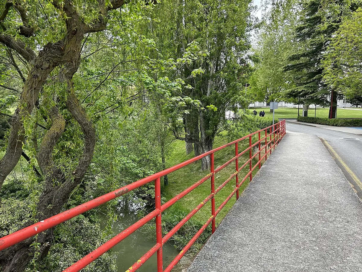 Petit pont à rambarde rouge sur un ruisseau arboré, campus de l’université de Navarre