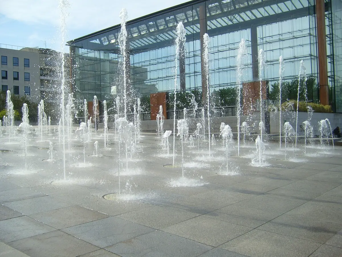 Les jets d’eau de la place devant un immeuble vitré