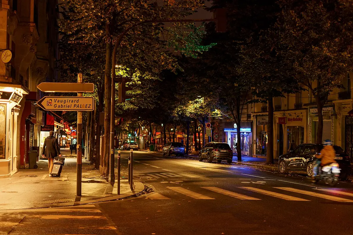 Une rue commerçante animée la nuit, avec voitures stationnées et un deux-roues, près de la rue d’Alleray