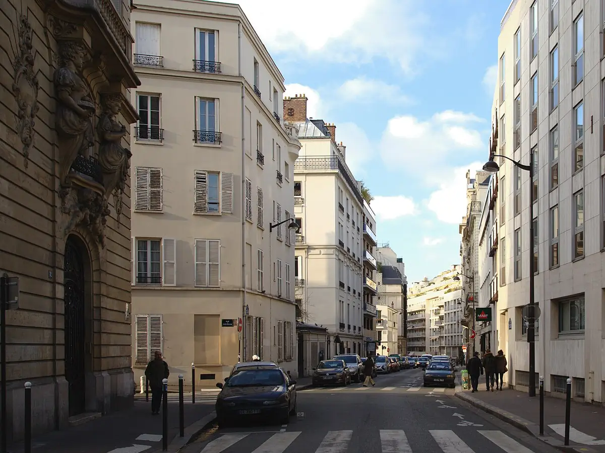 Une rue résidentielle tranquille avec une voiture garée et des façades anciennes