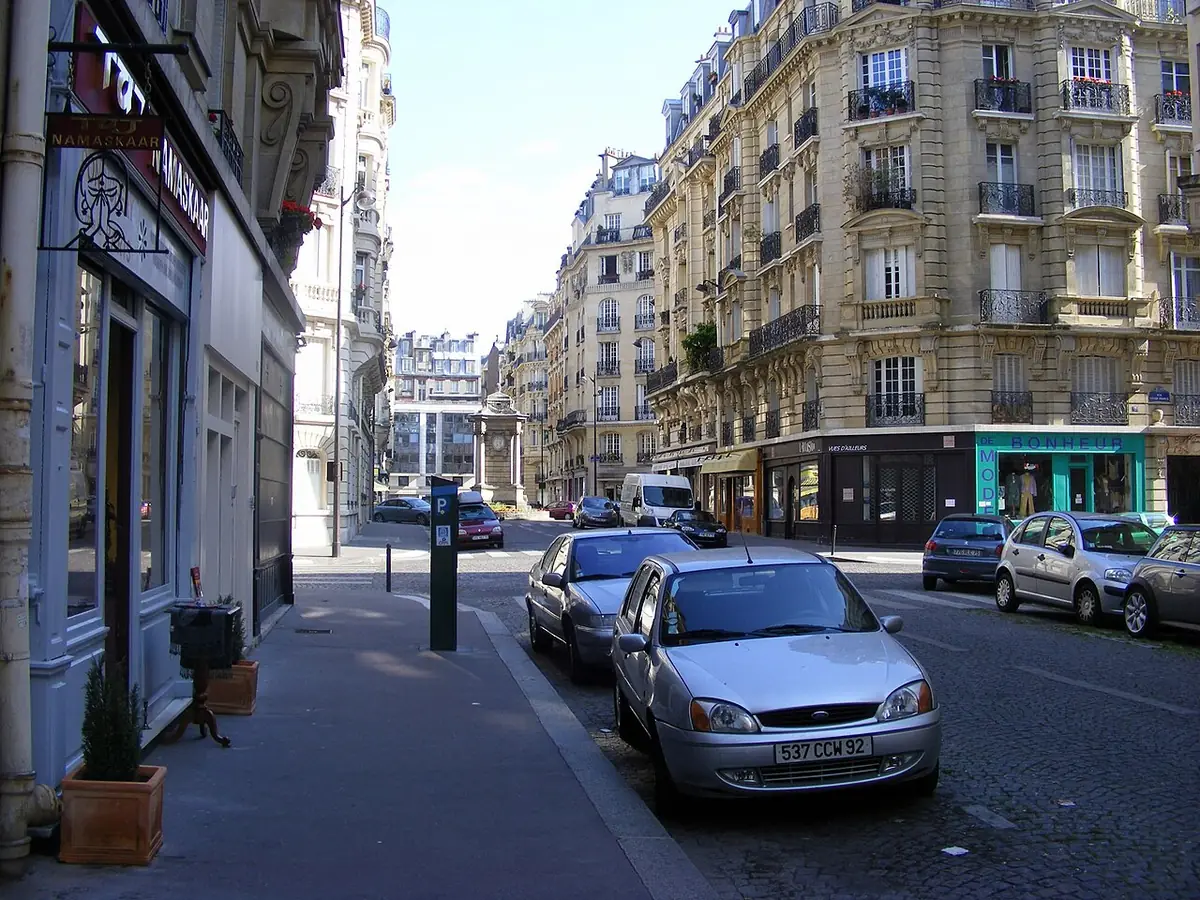 Une rue résidentielle bordée d’immeubles haussmanniens, voitures garées