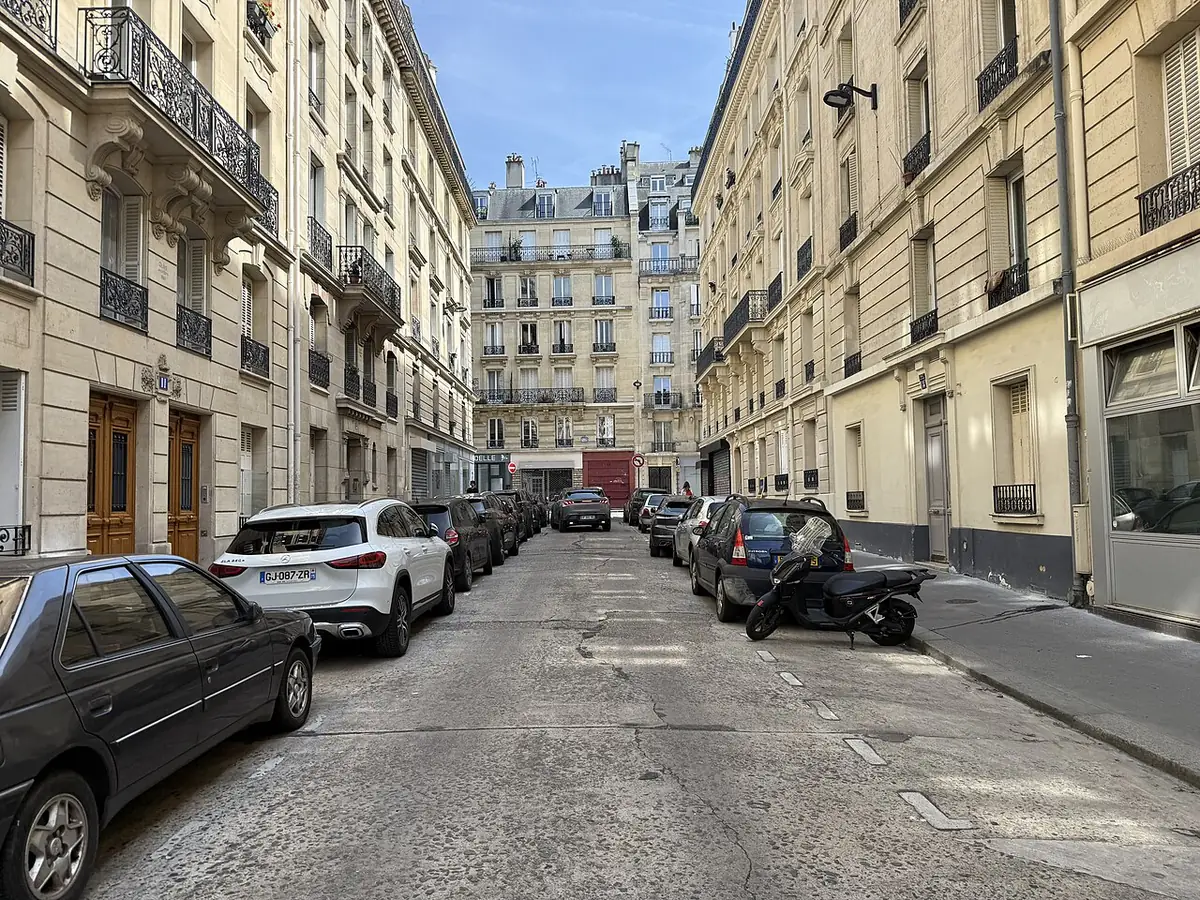 Une rue calme bordée de voitures garées et d’immeubles anciens