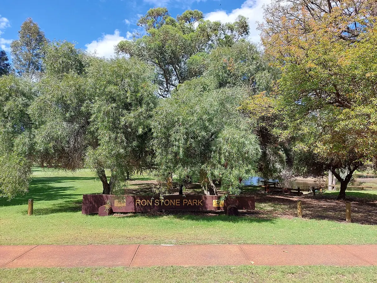 Panneau du Ron Stone Park sur une pelouse avec des arbres et un sentier rouge, sous un ciel bleu, à Mount Lawley, Perth